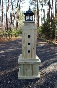 a wooden tower with a light on top in the middle of some gravel and trees