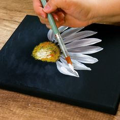 a person with a pen is painting a flower on a piece of black paper that has white feathers