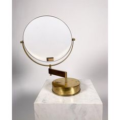 a round mirror sitting on top of a white marble block next to a gold plate