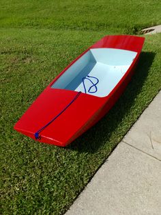 a red and white boat sitting on top of a green grass covered field next to a sidewalk