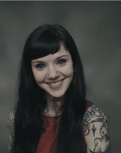 a woman with long black hair and tattoos on her chest smiles at the camera while wearing a red top