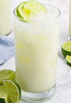 a glass filled with ice and limes on top of a white table next to two glasses