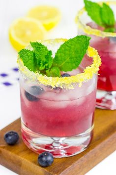 two glasses filled with blueberry lemonade and mint garnish on a cutting board