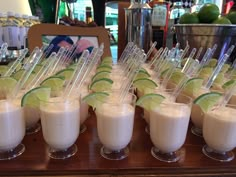 there are many drinks on the table with limes and straws in cups next to each other