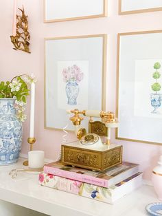 a white table topped with books and vases filled with flowers next to pictures on the wall