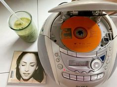 a cd player with an orange disk on top of it next to a glass of juice