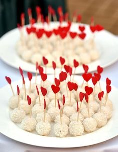 two white plates topped with desserts covered in red heart shaped candies and toothpicks