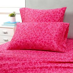 a bed with pink sheets and pillows on top of it next to a white nightstand