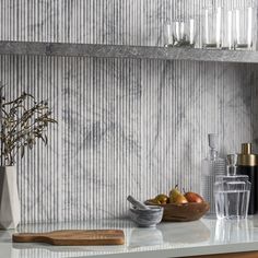 a marble kitchen counter top with some fruit and glasses on the shelf next to it