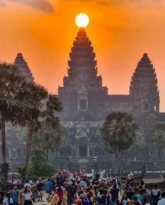 the sun is setting in front of an ornate building with palm trees and people walking around