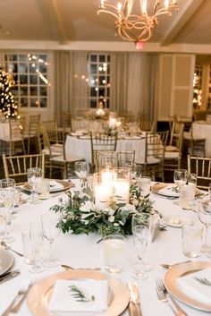 the table is set with white and gold plates, silverware, candles and greenery