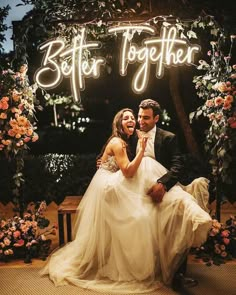 a bride and groom sitting under a neon sign that says better together in front of them