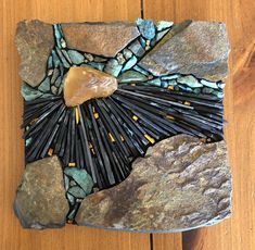 a piece of art made out of rocks and stones on a wooden surface with a heart shaped rock in the center