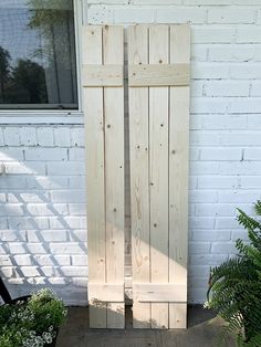 two wooden doors sitting next to each other in front of a white brick wall and green plants