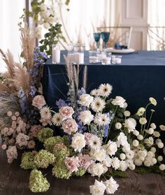 an arrangement of flowers and greenery on a table with a blue cloth draped over it