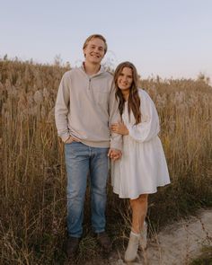 a man and woman standing next to each other in tall grass