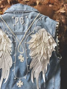 the back of a jean jacket with angel wings on it and pearls hanging from the chest