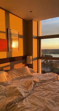 an unmade bed with white sheets and pillows in front of a large window overlooking the city