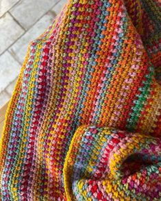 a multicolored crocheted blanket sitting on top of a wooden table next to a brick wall