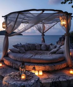 an outdoor bed with candles lit up on the ground and in front of water at dusk