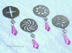 three earrings with different designs on them sitting on a white tablecloth, one is silver and the other has pink beads