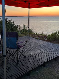 an umbrella and chair are set up on the deck overlooking the ocean at sunset or sunrise