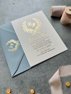 a blue and gold wedding card on top of a table next to spools of thread