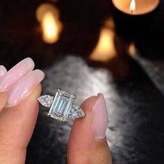 a woman's hand holding an engagement ring in front of a lit candlestick