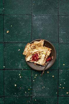 a plate with food on it sitting on a green tile floor next to a knife and fork