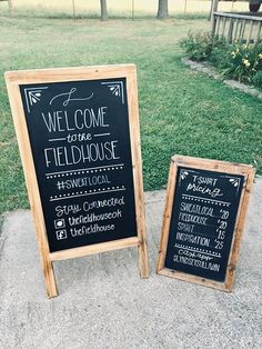 two chalkboard signs sitting next to each other in front of a grassy area with trees