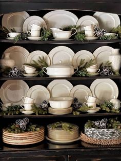 a black china cabinet filled with white dishes and christmas greenery on the top shelf