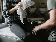 a man sitting on top of a kitchen counter next to a woman who is holding something in her hand