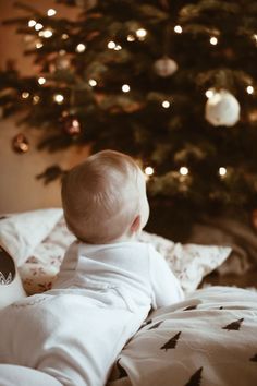 a baby sitting on top of a bed next to a christmas tree