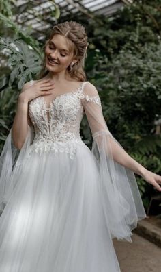 a woman in a white wedding dress is walking through the greenhouse with her arms outstretched