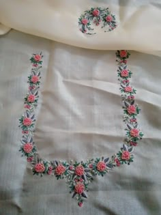 a necklace and earring are laying on a white sheet with pink flowers in the center