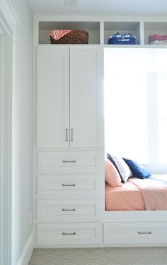 a bedroom with white built in storage units and a pink bedspread on the bed