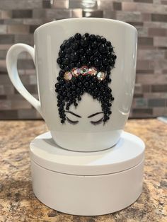 a white coffee cup with black beads on it's head and eyes, sitting on top of a counter