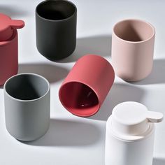 several different colored cups and containers on a white surface, with one empty cup in the middle