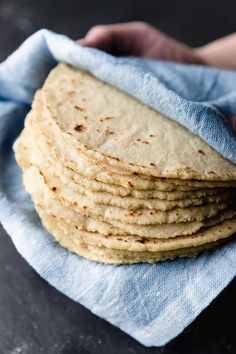 a stack of tortillas sitting on top of a blue cloth next to a person's hand