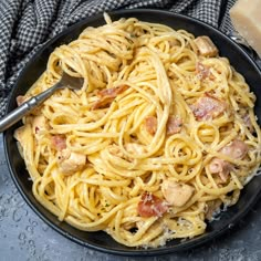 a black bowl filled with pasta and meat on top of a gray table next to a piece of bread