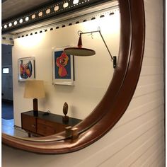 a round mirror hanging on the wall next to a lamp and table with a lamp shade