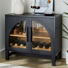 a black cabinet with wine glasses and bottles in it next to a potted plant