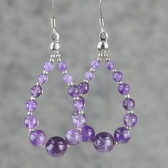 a pair of earrings with purple beads hanging from it's earwires on a gray background