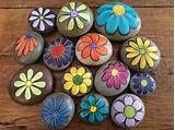 painted rocks with flowers on them sitting on a wooden surface