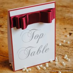 a top table card with a red bow on it and pearls scattered around the card