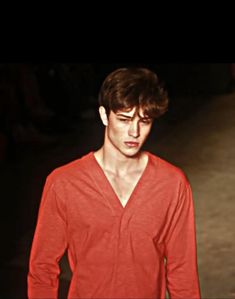 a young man in a red shirt is walking down the runway with his hand on his hip