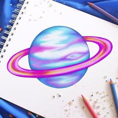 a spiral notebook with an image of the planet saturn drawn on it and colored pencils next to it