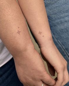 two people holding hands with small stars on their wrist tattooing one another's arm