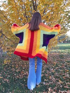 a woman standing in front of a tree wearing a multicolored knitted sweater