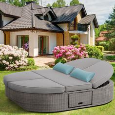 an outdoor chaise lounge with blue pillows in front of a large white and brown house